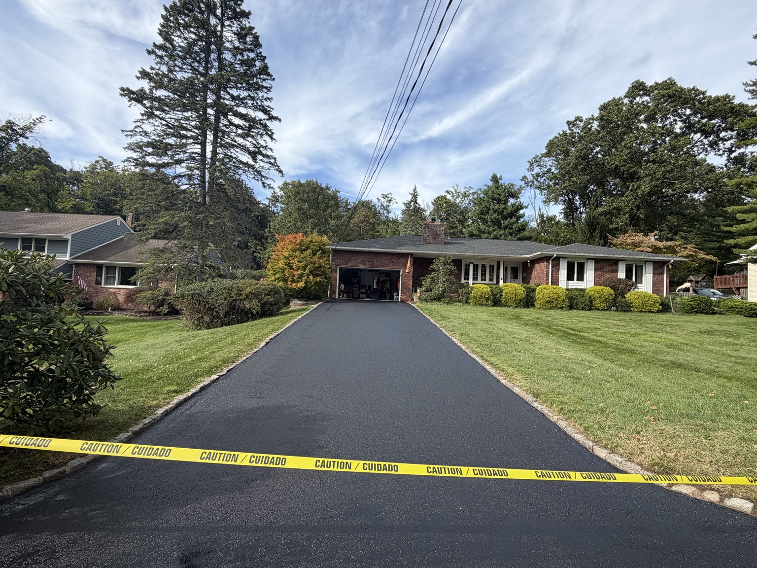 Same residential driveway freshly sealcoated, with caution tape across the entrance